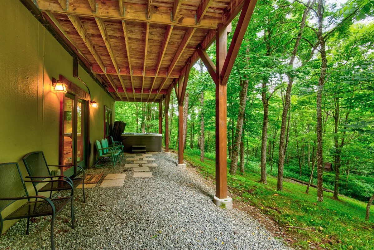 An exterior shot of the inviting hot tub area, framed by green chairs and wooden beams, sits in harmony with the surrounding landscape. The image conveys the perfect spot to unwind after a day of hiking or exploring, with hints of sunset and stargazing potential.