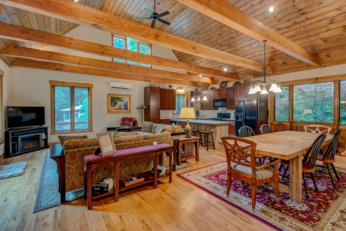 A welcoming great room with a comfortable sofa, large dining table, and a bright kitchen area. Expansive windows provide ample natural light and a view of the outdoors, while the overall ambiance is cozy and inviting, ideal for group activities and relaxation.