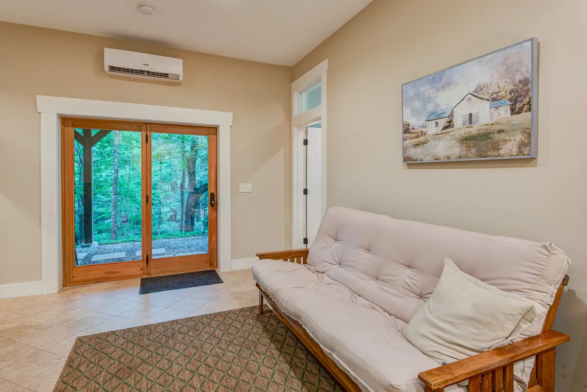 A cozy entertainment lounge with a futon sofa faces a glass door that opens to natural views. The space also features a painting on the wall, creating a relaxed and inviting atmosphere ideal for lounging, reading, or enjoying privacy.