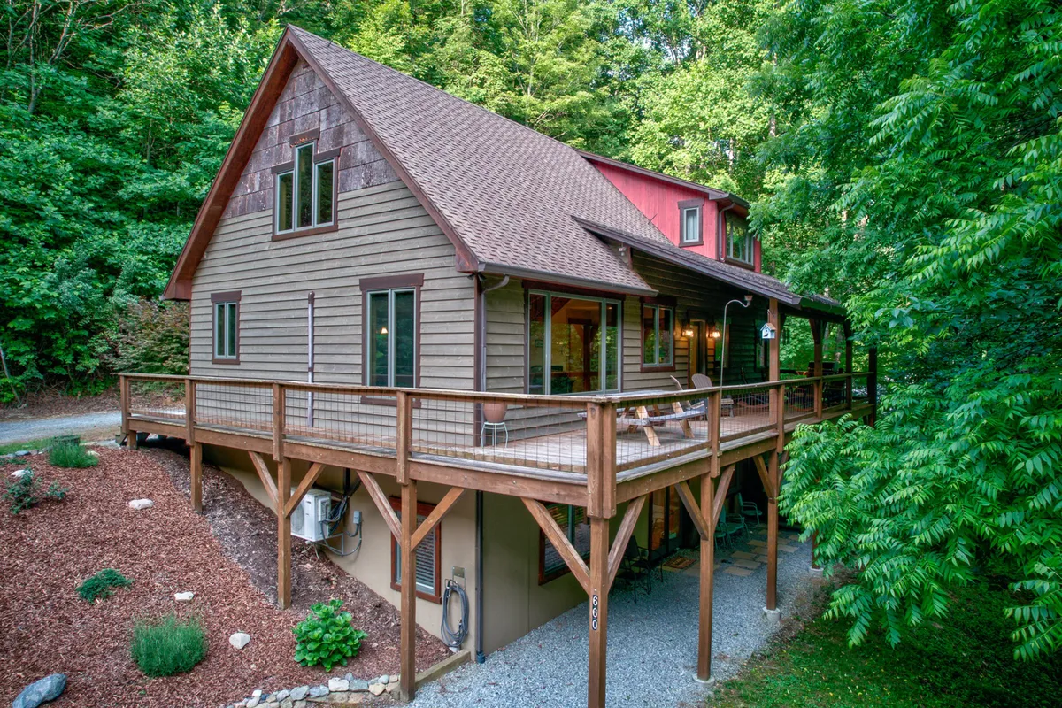 The image features the exterior of a spacious single-family home nestled in lush greenery, with a welcoming wooden deck perfect for outdoor dining and relaxation. The deck overlooks tranquil forest views, inviting guests to enjoy sunset moments or morning coffee in total privacy, surrounded by nature.