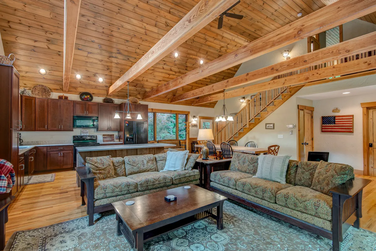 A comfortable gathering space with plush sofas, exposed wooden beams, a visible dining area, and kitchen. The arrangement is perfect for both relaxation and conversation, with cozy lighting and an inviting setup for group activities or unwinding by the fire.