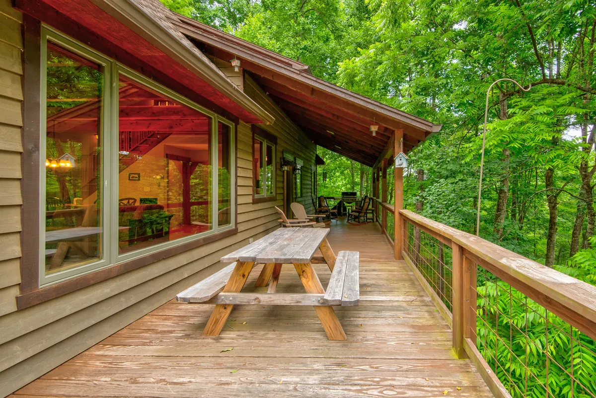 A welcoming outdoor dining area with a wooden picnic table sits beside large windows, surrounded by greenery. The setting is perfect for al fresco meals, group conversations, and evening stargazing, emphasizing a seamless connection between indoor comforts and the natural beauty that surrounds the home.